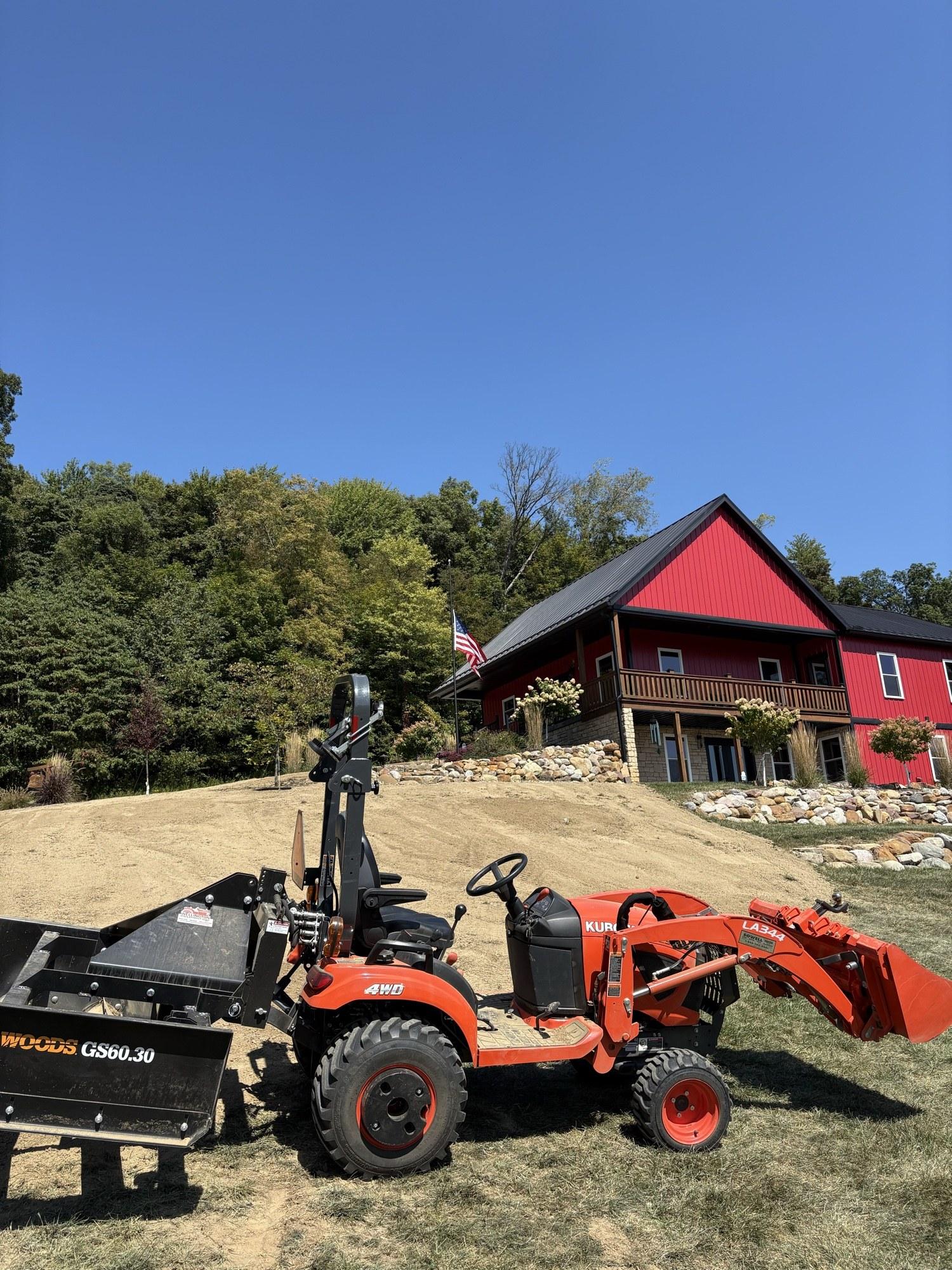 Compact tractor with a grading rake attachment preparing a soil pad for new lawn installation